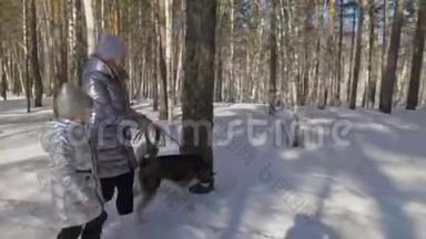 美丽的女人和<strong>小</strong>孩在冬天的森林里和哈士奇的狗散步。 快乐的年轻母亲和女儿